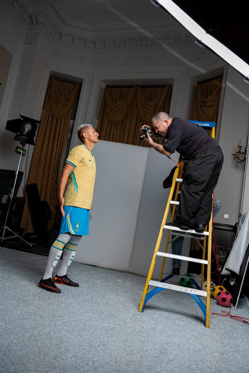 Photographer on a ladder shooting a player in the yellow Nike kit